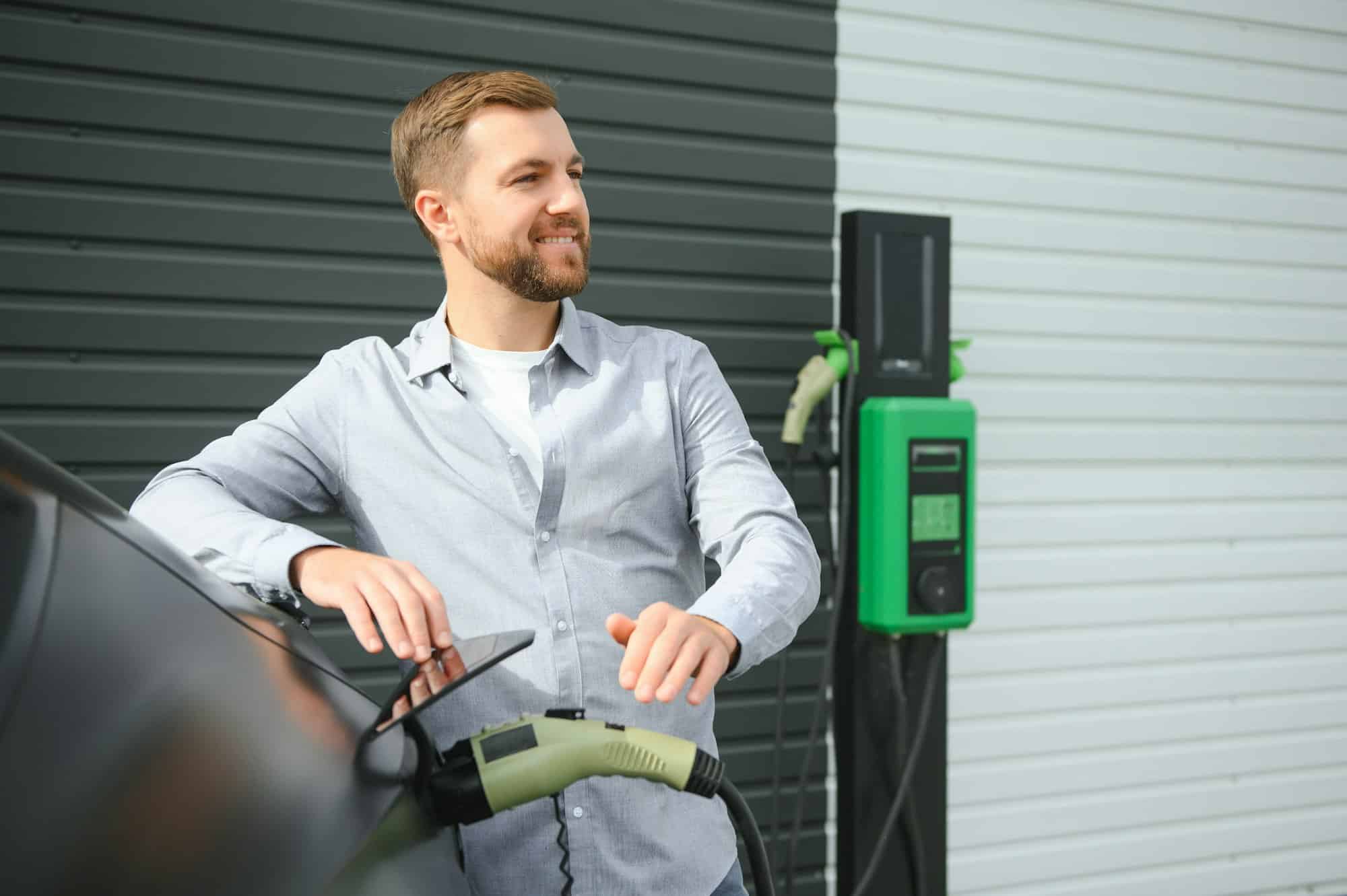Un homme se tient près d’une borne de recharge et recharge sa voiture électrique