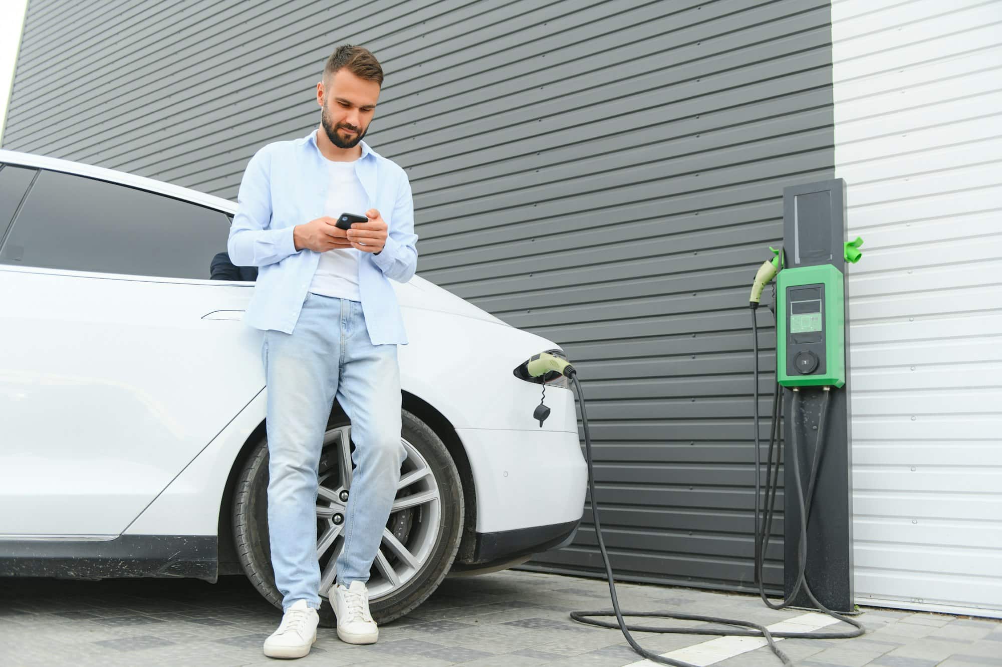 Homme heureux utilisant un téléphone intelligent et chargeant une voiture à la station de recharge du véhicule